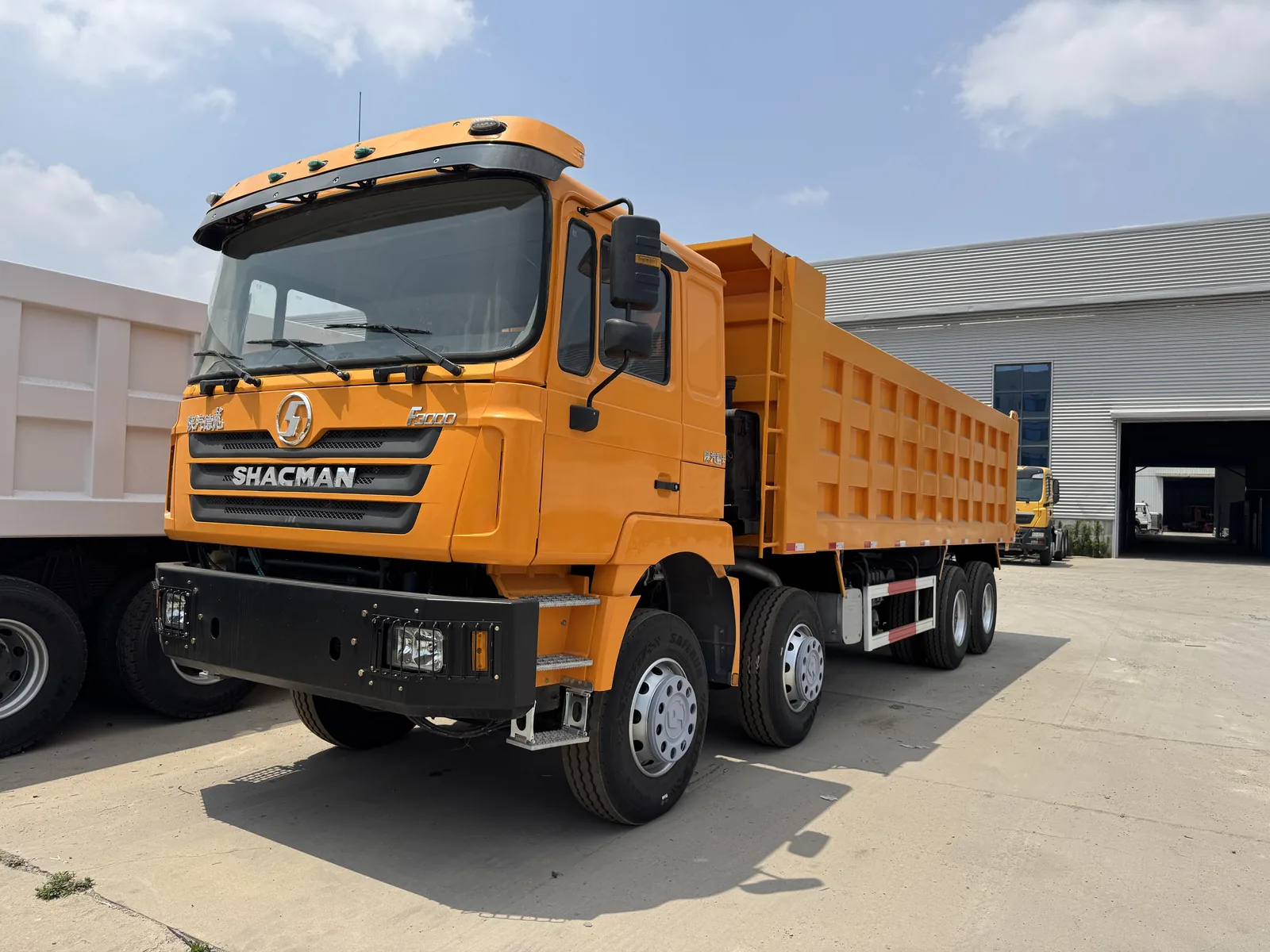 Front and side view of an orange SHACMAN dump truck